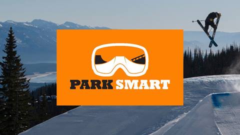 An orange Park Smart safety graphic, featuring a goggles icon, is overlaid on a photo of a skier catching air in a terrain park at Schweitzer.